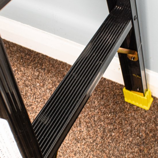 Detail van een zwart aluminium werkplatform met ribbels, met gele voetjes zichtbaar.