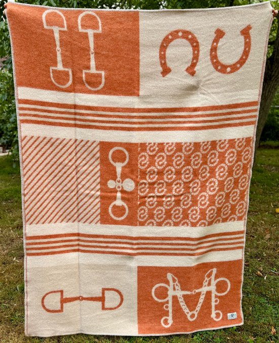 Oranje en crème wollen deken met paardrij-motieven zoals hoefijzers, bitten en een monogram. Met witte sierrand.