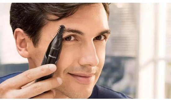 Een man trimt zijn wenkbrauwen met een zwarte Philips neus-, oor- en wenkbrauwtrimmer.