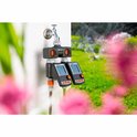 Gardena waterverdeler met kraan, twee slangen en twee digitale timers met oranje knoppen. Op de achtergrond een tuin.
