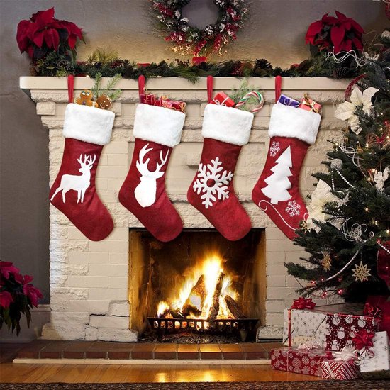 Quatre bas de Noël rouges à bords blancs et motifs de Noël: cerf, flocon de neige et arbre. Accrochés au-dessus d'une cheminée allumée.