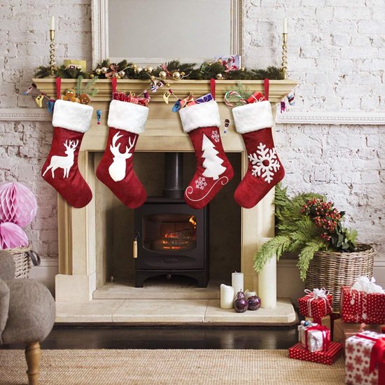 Quatre bas de Noël rouges à bords blancs et motifs de Noël: cerf, arbre et flocon de neige. Accrochés au-dessus d'une cheminée.