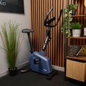 Marineblauwe hometrainer met 'TREX SPORT' logo in een fitnessruimte met planten.
