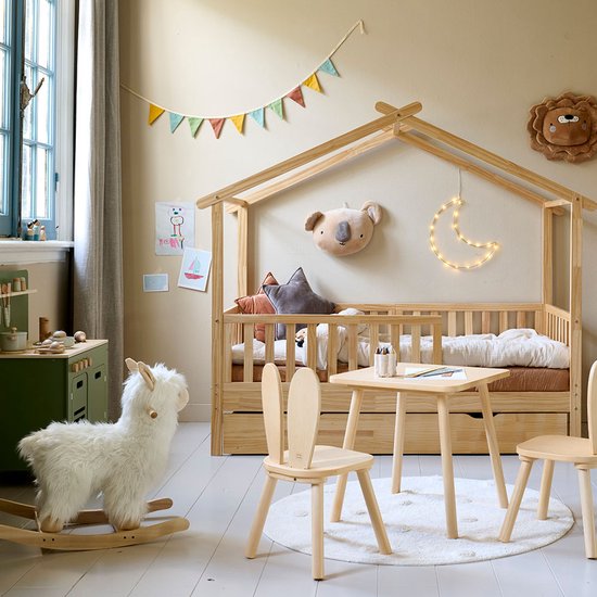 Wit Alpaca hobbelpaard in een kinderkamer, naast een houten tafel en stoelen.