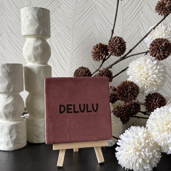 Rood tegeltje met de tekst "DELULU" op een mini schildersezel.
