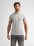 Man met krullend haar draagt een effen lichtgrijs T-shirt met ronde hals en grijze jeans.