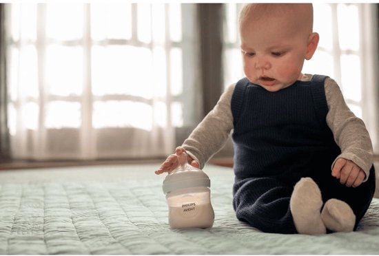 Bébé assis par terre, regardant un biberon Philips Avent Natural Response.