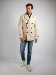 Man draagt crèmekleurige wollen peacoat, spijkerbroek en crèmekleurige sneakers.