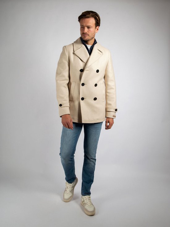 Man draagt crèmekleurige wollen peacoat, spijkerbroek en crèmekleurige sneakers.