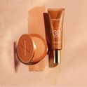 Lancaster tube met SPF 30 en poederdoosje met foundation, naast vegen foundation.