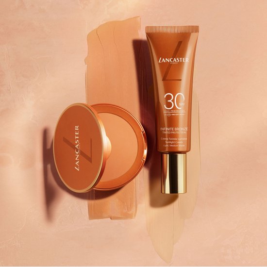 Lancaster tube met SPF 30 en poederdoosje met foundation, naast vegen foundation.