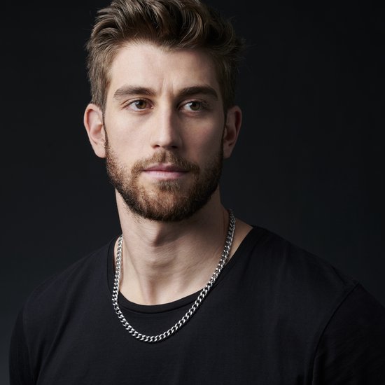 Man met stoppels, zwart T-shirt en een zilverkleurige schakelketting.