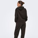 Model staat met de rug naar de camera, handen in de zakken, in een donkerbruine hoodie.
