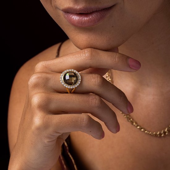 Femme portant une bague dorée avec une grande citrine fumée facettée et des cristaux.