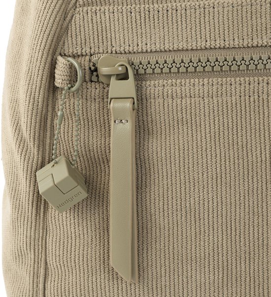 Close-up van beige ribfluwelen rugzak met rits, label en een vierkant bedeltje met 'Hedgren'.