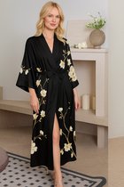 Volledige outfit van een vrouw in een lange zwarte kimono met magnolia print, met gouden oorbellen en hakken.
