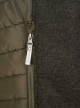 Sluiting met rits en schuifje met logo op een olijfgroene gewatteerde bodywarmer met donkergrijs gebreide zijkanten.
