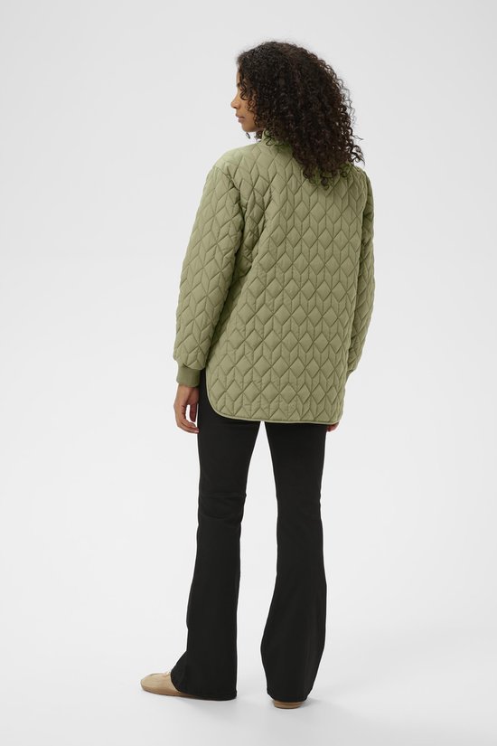 Achterkant van een vrouw in olijfgroene, doorgestikte jas met rits en zwarte broek.