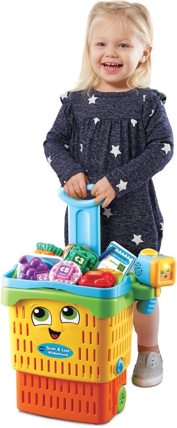 Blond meisje in blauw jurkje met witte sterren, duwt een felgekleurde winkelwagen met speelgoedboodschappen.