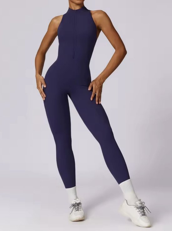 Donkerblauwe, mouwloze jumpsuit met hoge nek, rits aan de voorzijde en witte sportsokken.