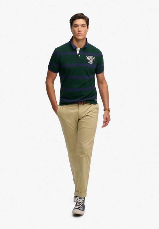 Man lopend, draagt een donkergroene polo met marineblauwe strepen en geborduurd logo.