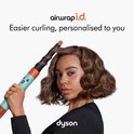Vrouw met bruin, golvend haar krult met Dyson Airwrap i.d. in de kleuren blauw en oranje.