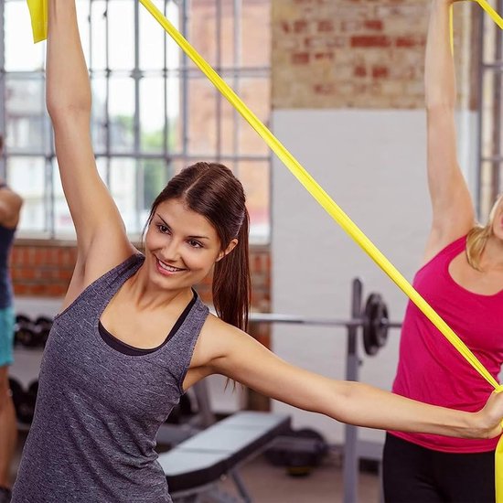 Twee vrouwen trainen met gele weerstandsbanden in een fitnessruimte.