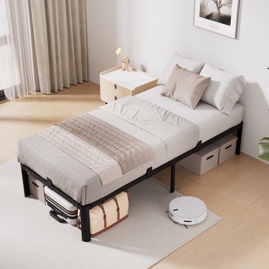 Een opgemaakt zwart metalen bedframe in een slaapkamer, met opbergkoffers eronder. Een robotstofzuiger staat naast het bed.