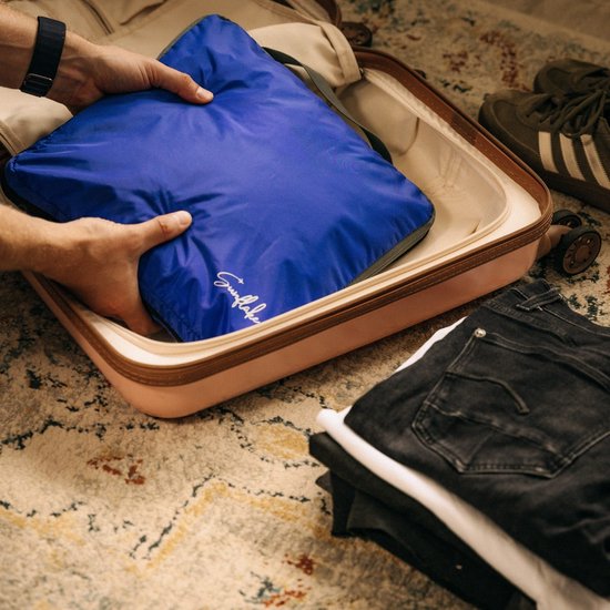Blauwe Sunflake packing cube wordt in een roze koffer gelegd, naast kleding en schoenen.