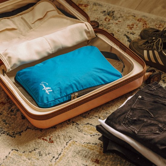 Blauwe Sunflake packing cube in een opengemaakte koffer, naast kleding.