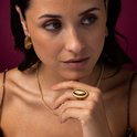 Close-up van een model die een gouden ring met een ovaal tijgeroog en gouden oorringen draagt. De ring is een statement.