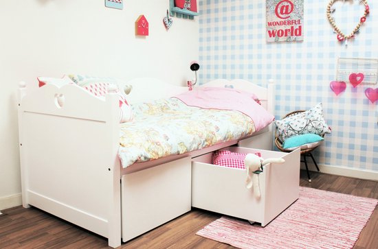 Wit bed met lades, gedecoreerd met hartjes, en een stoel met kussens.