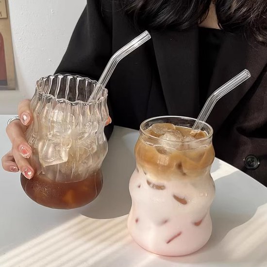 Twee gegolfde glazen bekers met rietjes. Eén met ijskoffie, de ander met roze drank.