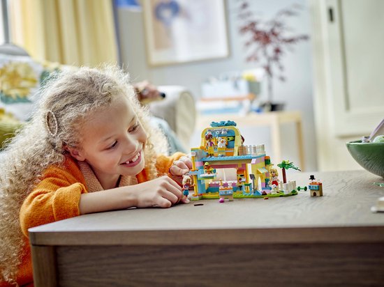 Une fille aux cheveux bouclés joue avec l'animalerie LEGO Friends sur une table en bois. La boutique est violette, jaune, bleue et rose.