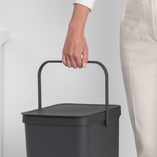 Main d'une femme tenant la poignée incurvée d'une poubelle grise.