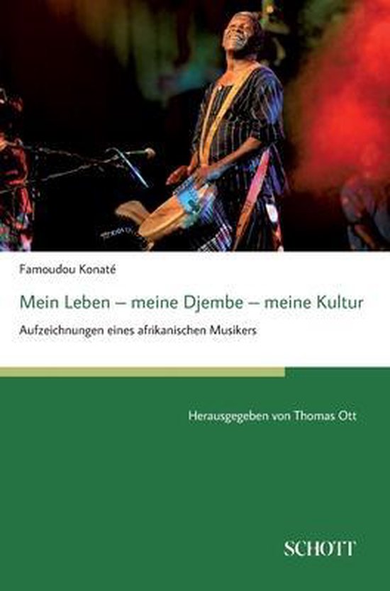 Famoudou Konaté, bespeelt een djembe op een podium. Zwart-wit gestreept shirt.