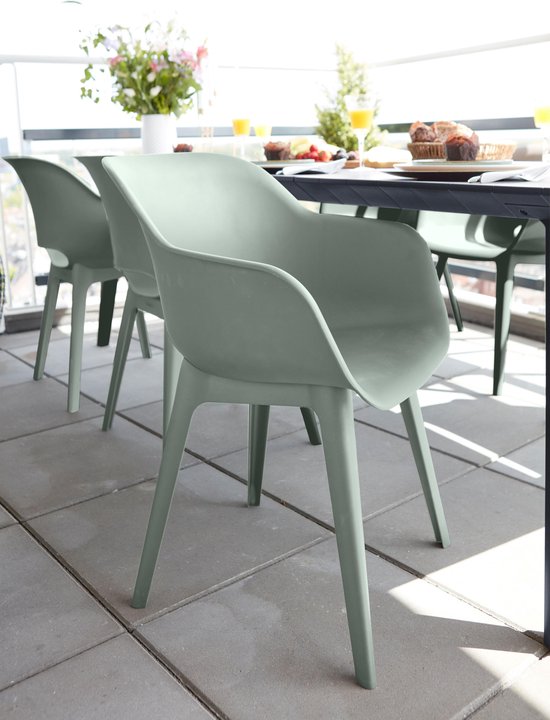 Une chaise de jardin vert vintage à une table de jardin avec nourriture et fleurs, sur une terrasse pavée.