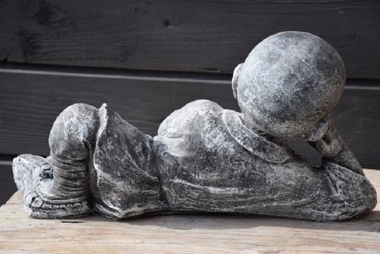 Figurine grise en béton d'un jeune moine couché sur le ventre, le dos tourné au spectateur.