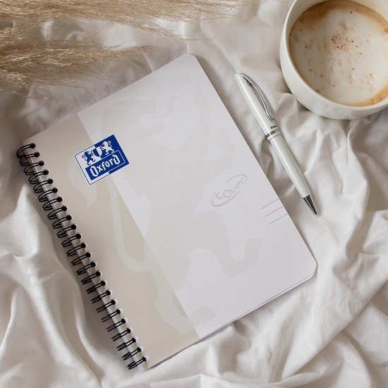 Lichtgrijs Oxford notitieboek met spiraalbinding op een wit laken, naast een kopje koffie en een witte pen.