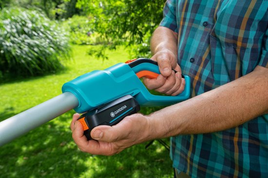 Man plaatst oranje/zwarte GARDENA batterij in turquoise heggenschaar.