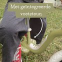 Close-up van een kind op een lichtgroene loopfiets met geïntegreerde voetsteun.