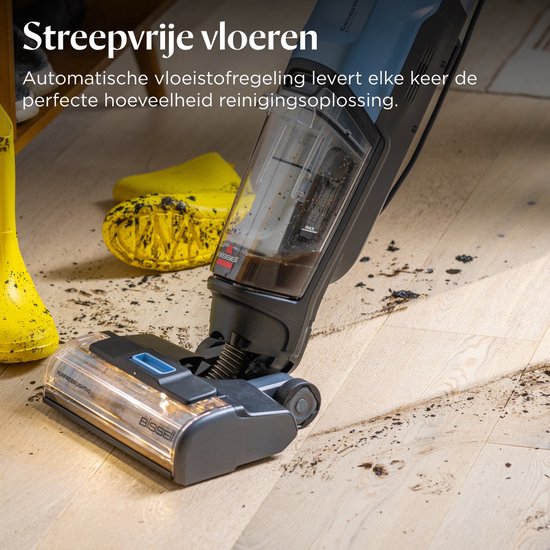 Een stofzuiger met ledverlichting bij de borstelkop zuigt vuil op van een houten vloer. Een paar gele laarzen liggen ernaast.