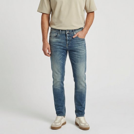 Man draagt een blauwe spijkerbroek met lichte wassing, slim fit model. Knoopsluiting en steekzakken.