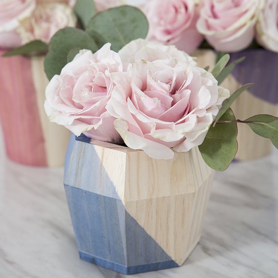 Houten vaas met geometrisch design, gedeeltelijk geverfd in blauw en paars, met roze rozen en eucalyptusbladeren.