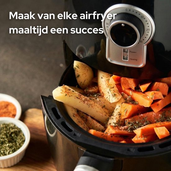 Close-up van een airfryer gevuld met aardappelpartjes en worteltjes, bestrooid met kruiden.