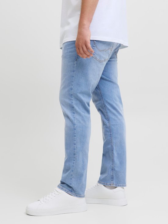 Man draagt een witte T-shirt en een lichtblauwe spijkerbroek, van de zijkant gezien.