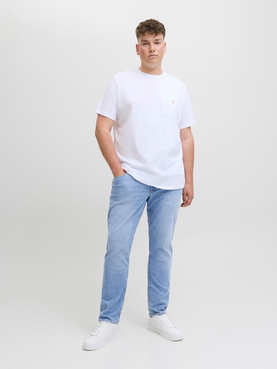 Man draagt een witte T-shirt met opgestoken zak en een lichtblauwe spijkerbroek, van voren gezien.