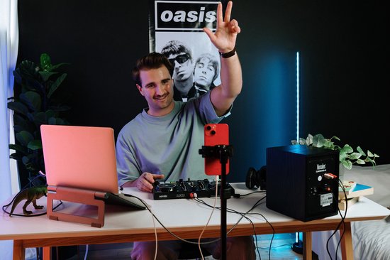 Man met Oasis poster in de achtergrond, draait DJ set met Hercules controller op een bureau.