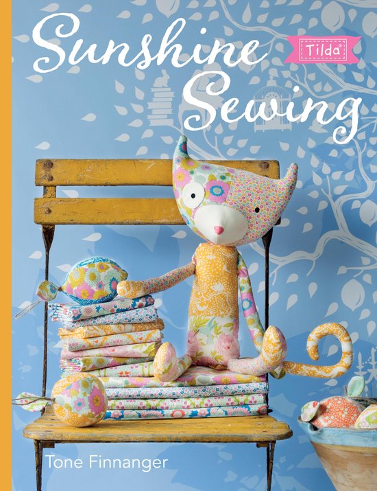 Boekhoes "Sunshine Sewing" met een vrolijke, stoffen kat met bloemenpatroon en een stapel stoffen.