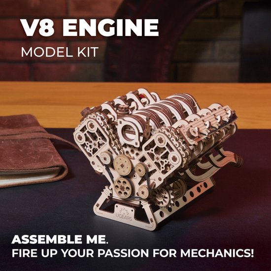 Gedetailleerd houten V8-motor model op een bureau naast een notitieboek. Tekst: V8 ENGINE MODEL KIT.